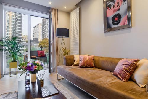 a living room with a brown couch and a large window at Lumina apartments near Warsaw Uprising Museum in Warsaw