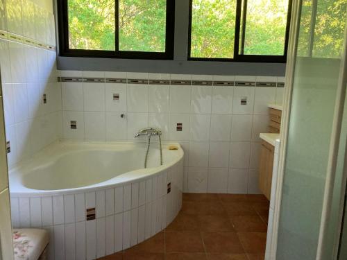 - une salle de bains blanche avec baignoire et 2 fenêtres dans l'établissement maison dans les landes avec piscine, à Trensacq