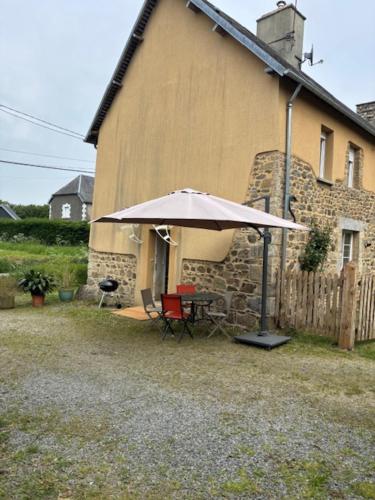 une table avec un parasol devant un bâtiment dans l'établissement Maison normande tout confort, à Saint-Michel-de-la-Pierre