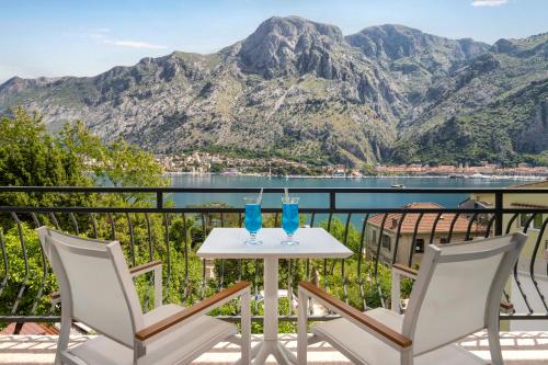 a table with two glasses on a balcony with mountains at Apartments Dončić in Kotor