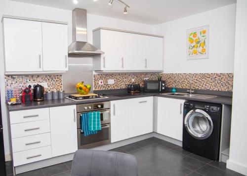 a kitchen with white cabinets and a washing machine at Lavish 4-Bedrooms with Modern Home Features - Sleeps 8 - Hi-Speed Wi-Fi - Luxury Garden - Private Ample Parking in Peterborough
