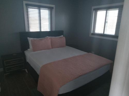 a bedroom with a bed with pink pillows and two windows at Vacation Haven Cottages in Rolleville