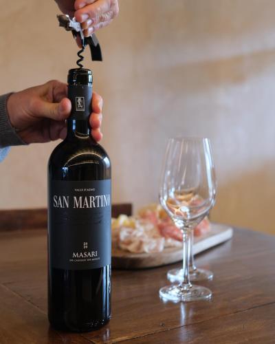 a person opening a bottle of wine next to a glass at MASARI ALLA CASA ROSSA Vineyard guest house in Brogliano