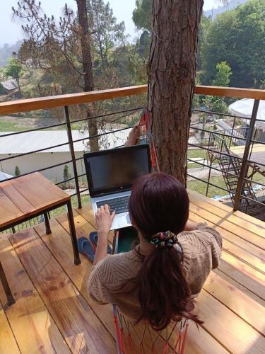 a woman sitting in a hammock with a laptop on a deck at Paradise Pool Resort in Nainital