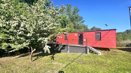 a red tiny house in a field with a tree at Gabčíkovo - Prístav in Gabčíkovo
