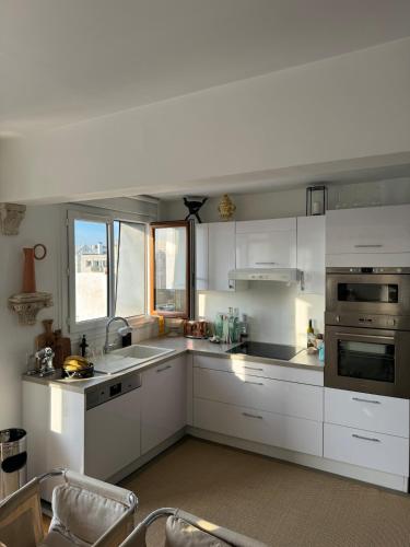 une cuisine avec des placards blancs et une grande fenêtre dans l'établissement Appartement canal saint Martin, à Paris