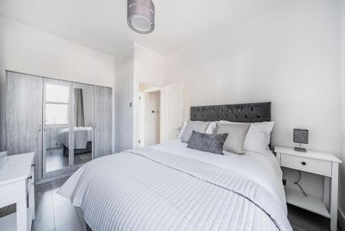 a white bedroom with a large bed and a mirror at Amazing One Bed Flat Wimbledon in London