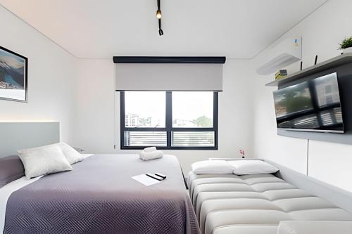 a white room with two beds and a tv at Apartamentos modernos próximo ao Jardim Botanico e à Rodoviária in Curitiba