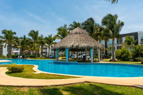 a swimming pool with a straw umbrella and palm trees at Beautiful Apartment in Dream Acapulco Diamante in Acapulco