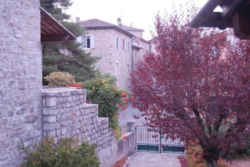 a house with a stone wall and a red tree at MAS DUMAS - Maison de village en pierre avec jardin privé in Chandolas