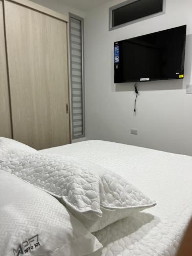 a white bed with a flat screen tv on the wall at Apartahotel Centro 101 Edificio PF7 primer piso in Pitalito