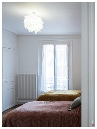 - une chambre blanche avec 2 lits et un lustre dans l'établissement Terrasse 4P - 16 min Paris - Bois de Vincennes 700m, à Charenton-le-Pont