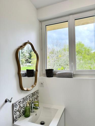 ein Badezimmer mit einem Waschbecken und einem Spiegel sowie zwei Fenstern in der Unterkunft Villa Cornelia Bagnoles Mezzanine Confort & Nature in Bagnoles de l'Orne