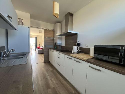 une cuisine avec des armoires blanches, un évier et un micro-ondes dans l'établissement Appartement T3 moderne avec terrasse et vue mer - Le Lavandou - FR-1-308-208, au Lavandou