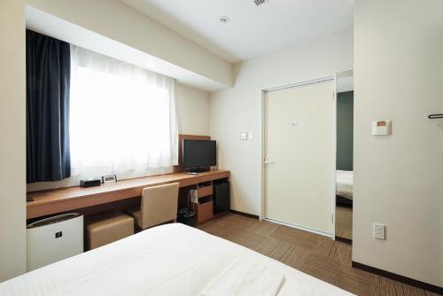 a bedroom with a bed and a desk with a television at キップホテル湘南藤沢 in Kugenuma