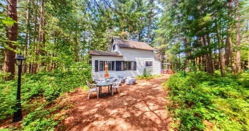 a small white cabin in the middle of a forest at Stabbin Cabin #2 on Grant Island - Hot Tub, Boat, Pet Friendly in Glenfield