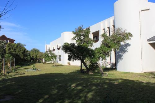 a white building with a tree in front of it at Grand Yellow Apartment in Port Alfred