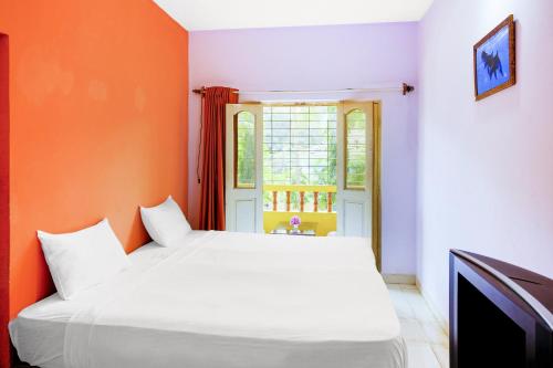 a bedroom with a white bed and an orange wall at Hotel O Mahamaya Holiday Inn in Goa