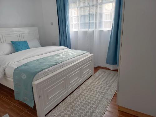 a bedroom with a white bed and a window at The Kioka gardens 4 bedroom home in Nanyuki