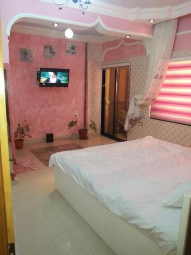 a bedroom with a bed and a tv on a pink wall at Z apartment in Az Zarqa