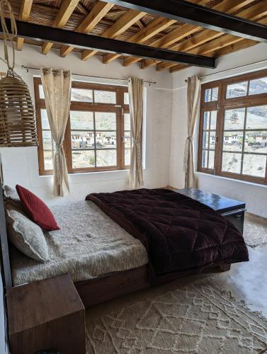 a bedroom with a large bed in a room with windows at Spiti Sojourn - Homestay at the Edge in Kaza
