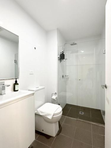 a white bathroom with a toilet and a shower at Super Convenient 1BR Apt Free Parking & study in Sydney