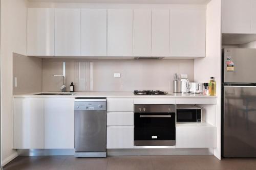 Una cocina con gabinetes blancos y electrodomésticos de acero inoxidable. en Super Convenient 1BR Apt Free Parking & study, en Sídney