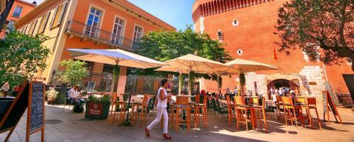 a man walking past an outdoor cafe with tables and umbrellas at L Oranger in Rivesaltes