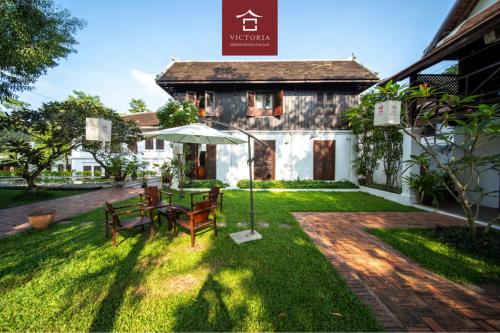 a patio with a table and an umbrella in front of a house at Victoria XiengThong Palace in Luang Prabang