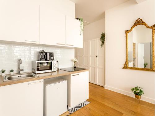 La cuisine est équipée de placards blancs, d'un lavabo et d'un miroir. dans l'établissement Merveil - Family Suite - Louvre - Sentier I, à Paris