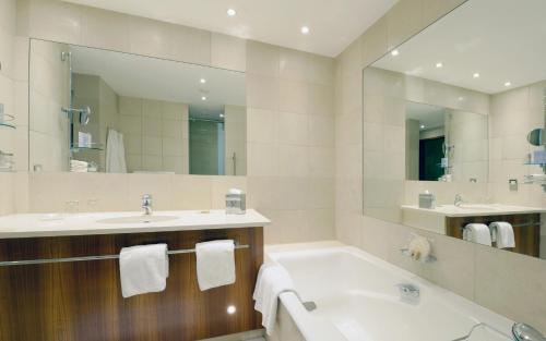 a bathroom with a tub and a sink and a mirror at Canary Riverside Plaza Hotel in London