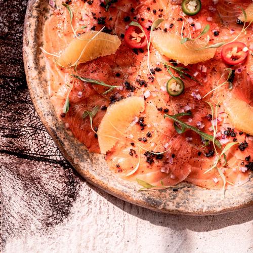 a pizza with fish and oranges on a table at ME Cabo by Meliá in Cabo San Lucas