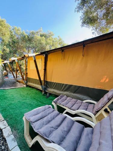 two chairs and two beds on a lawn with a tent at Camper Village in Santo Stefano al Mare