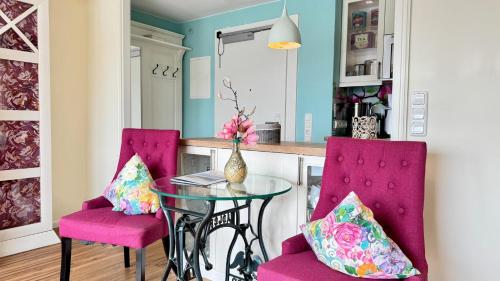 a kitchen with a glass table and two pink chairs at 6-401, Extravagante Strandwohnung, Art Nouveau meets französischen Landhausstil! 1Zimmer in Westerland (Sylt)