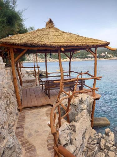 a wooden gazebo with a bench on the water at Apartmani Nikola in Zastražišće
