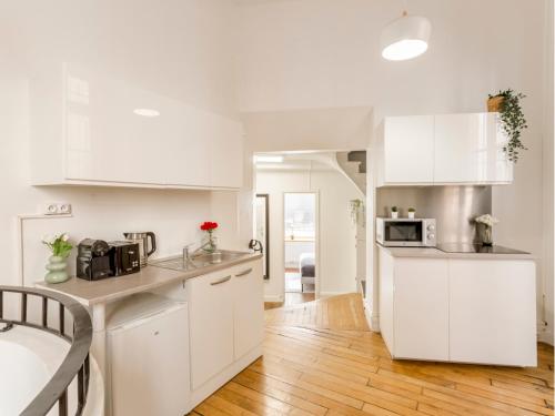 Il comprend une cuisine blanche avec des placards blancs et du parquet. dans l'établissement Merveil - Family Suite - Louvre - Clery, à Paris