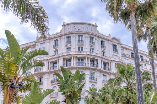 un grand bâtiment blanc avec des palmiers devant dans l'établissement Croisette 65 apartment-Miramar residence, à Cannes