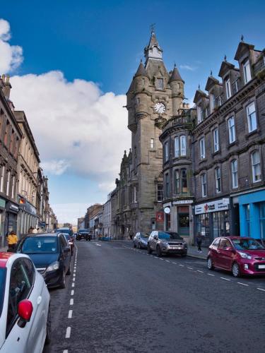a city street with a clock tower and cars parked at Cosy Ground Floor Victorian Flat in the Heart of Hawick in Hawick