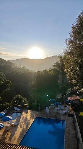 a view of a swimming pool with umbrellas and the sunset at Chalés Vila da Serra in Serra Negra