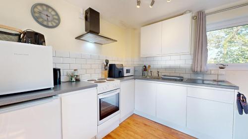 a kitchen with white cabinets and a clock on the wall at Bryntin in Penzance