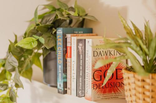 a row of books sitting on a shelf with plants at Elevated Ocean View Oasis - 3BR 2 Bath Parking in Christchurch