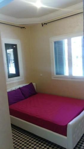 a room with a bed with purple sheets and two windows at Etablissement moderne in Safi