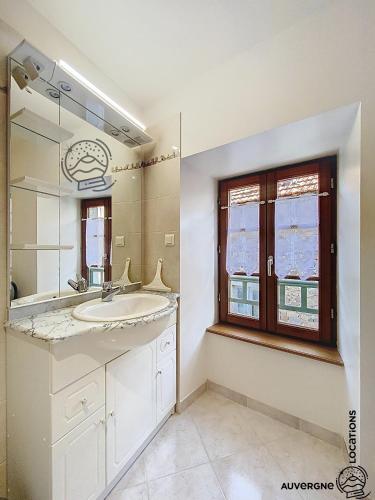 une salle de bain avec un lavabo, un miroir et une fenêtre dans l'établissement La Petite Barriade, à Saint-Nectaire