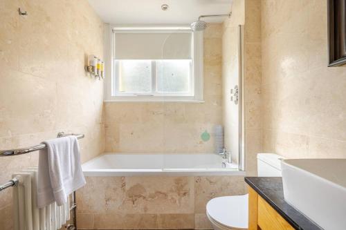 Un baño con bañera, inodoro y ventana. en Classroom Flat Suite in a converted school in Fowey town centre, en Fowey