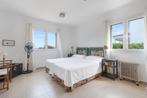 een witte slaapkamer met een bed en twee ramen bij Villa Tres in Es Mercadal