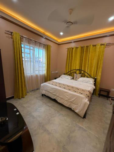 a bedroom with a bed with yellow curtains and a tv at Heavenly ApHEARTment with backyard swimming pool in Dodoma