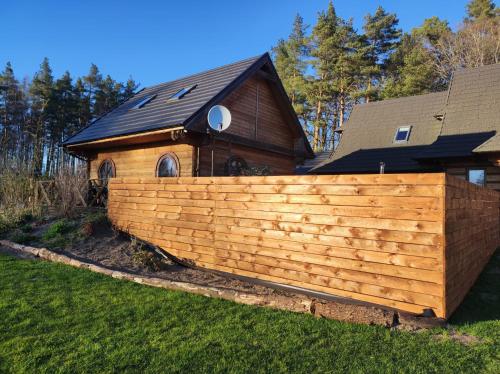 a wooden fence in front of a house at Woodorf drewnem usłane - domki z bala nad rzeką Słupią wśród pól i lasów z chatą grillową, ogniskiem i placami zabaw dla dzieci -Royal Red House z jacuzzi i ogrodzonym extra ogródkiem dla piesków, Royal Green House - bez jacuzzi in Ustka