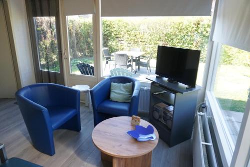 a living room with blue chairs and a tv and a table at Kustverhuur, Park Schoneveld, Duinroos 099 in Breskens