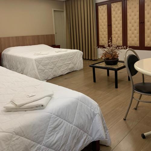 two beds in a hotel room with a table and chairs at Gran Lord Hotel in Pará de Minas