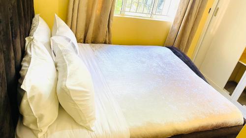 a bed with white sheets and pillows with a window at Spacious City Home in Kampala